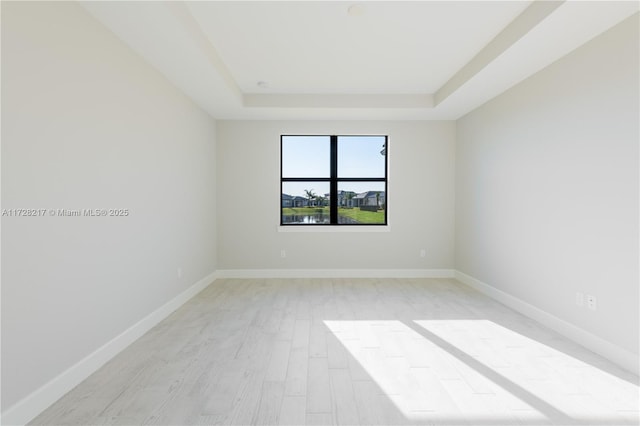 empty room with a tray ceiling, light wood-style floors, and baseboards