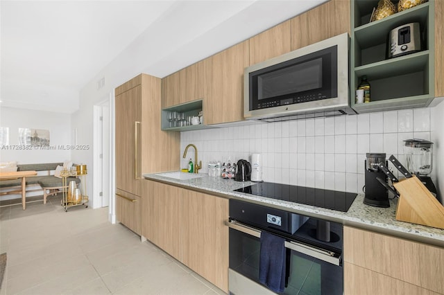 kitchen with light stone countertops, black electric stovetop, sink, backsplash, and oven