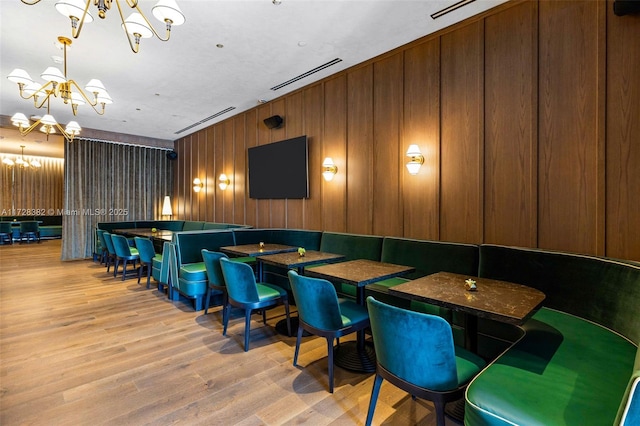 interior space featuring light wood-type flooring, wooden walls, and an inviting chandelier