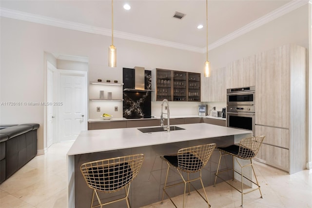 kitchen with ornamental molding, sink, hanging light fixtures, and a kitchen island with sink