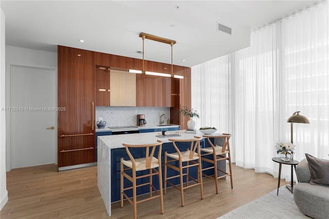 kitchen featuring a kitchen breakfast bar, decorative light fixtures, backsplash, a kitchen island with sink, and light hardwood / wood-style floors