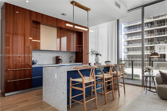 kitchen with a wall of windows, decorative backsplash, light wood-type flooring, decorative light fixtures, and a center island with sink