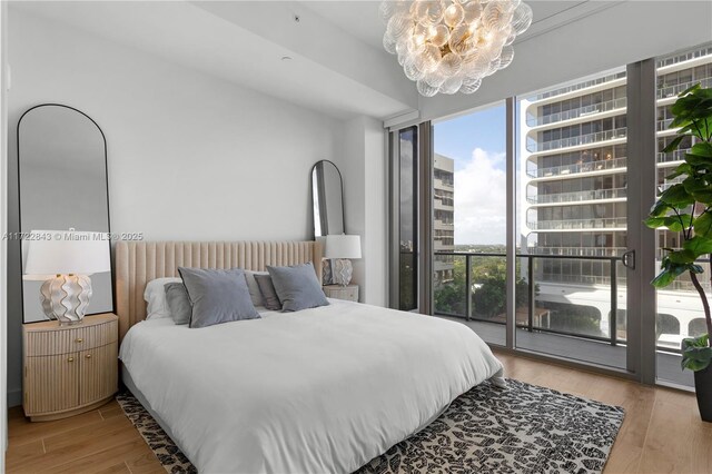 bedroom with a chandelier, light wood-type flooring, access to exterior, and expansive windows