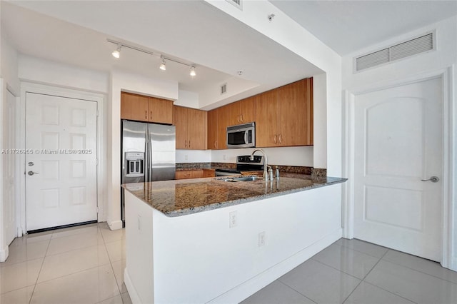 kitchen featuring light tile patterned floors, kitchen peninsula, stainless steel appliances, dark stone counters, and sink