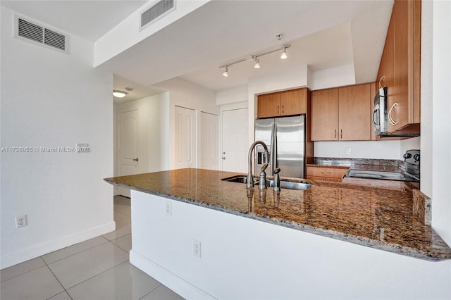 kitchen featuring appliances with stainless steel finishes, dark stone countertops, kitchen peninsula, and sink