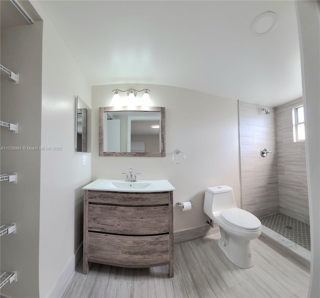 bathroom with hardwood / wood-style flooring, toilet, vanity, and a tile shower