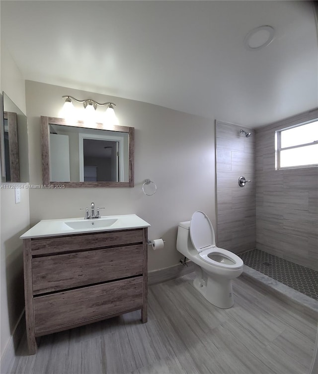 bathroom featuring toilet, vanity, tiled shower, and hardwood / wood-style flooring