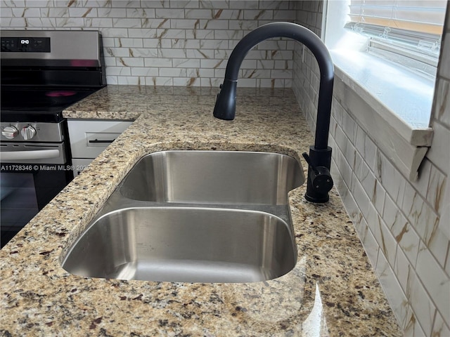 details with stainless steel range with electric cooktop, light stone countertops, sink, and decorative backsplash