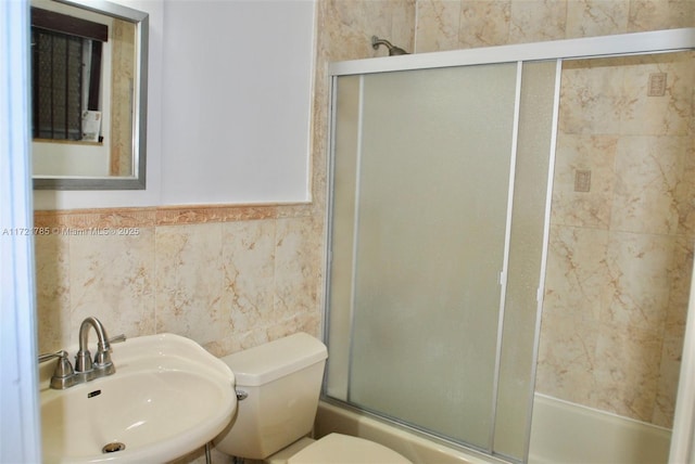 full bathroom with sink, tile walls, combined bath / shower with glass door, and toilet