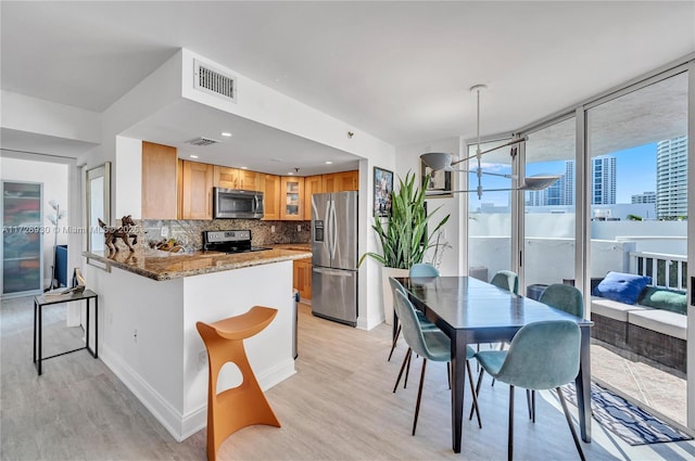 kitchen featuring kitchen peninsula, stainless steel appliances, decorative backsplash, stone countertops, and hanging light fixtures