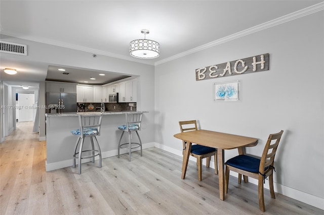 dining area with light wood-type flooring, baseboards, visible vents, and crown molding