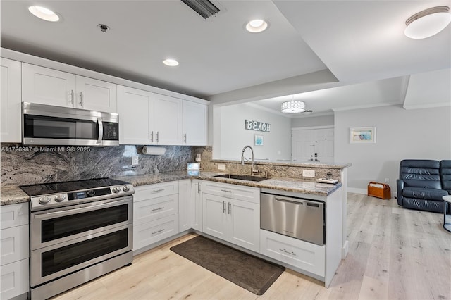 kitchen featuring a peninsula, appliances with stainless steel finishes, a sink, and white cabinetry