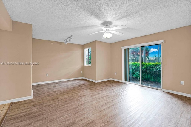 empty room featuring ceiling fan, hardwood / wood-style floors, track lighting, and a healthy amount of sunlight