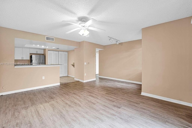 unfurnished living room with light wood-type flooring, ceiling fan, track lighting, and a textured ceiling