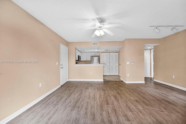 unfurnished living room with a textured ceiling, ceiling fan, rail lighting, and light hardwood / wood-style flooring