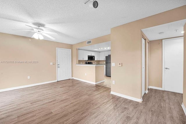 unfurnished living room featuring ceiling fan, a textured ceiling, and light hardwood / wood-style flooring