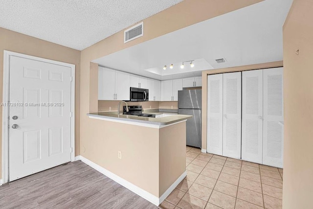 kitchen with kitchen peninsula, light tile patterned flooring, stainless steel appliances, a textured ceiling, and white cabinets