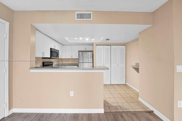 kitchen featuring white cabinetry, appliances with stainless steel finishes, kitchen peninsula, and a textured ceiling