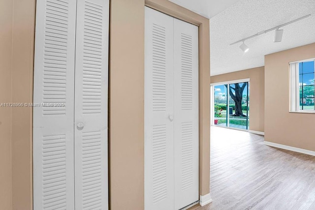 hallway with a textured ceiling, rail lighting, and light hardwood / wood-style floors