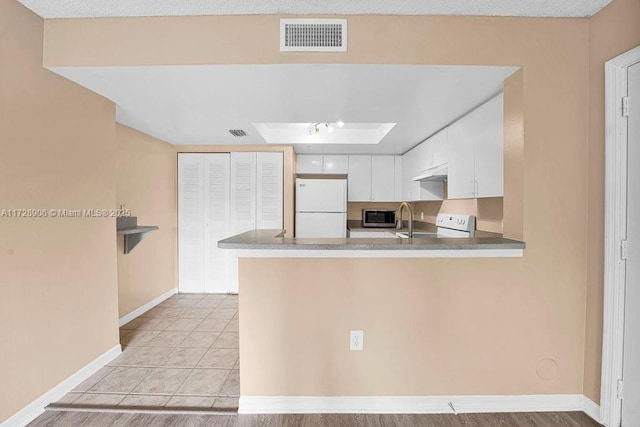 kitchen featuring white cabinets, kitchen peninsula, and white appliances