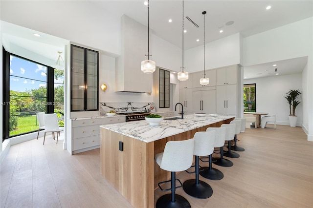 11001 SW 74th Ave, Pinecrest, FL 33156 - kitchen with a sink, light wood-style flooring, a large island, a towering ceiling, and glass insert cabinets