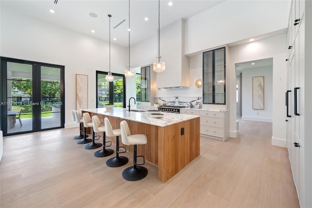 11001 SW 74th Ave, Pinecrest, FL 33156 - kitchen featuring a high ceiling, a large island with sink, light wood-style flooring, french doors, and light stone countertops