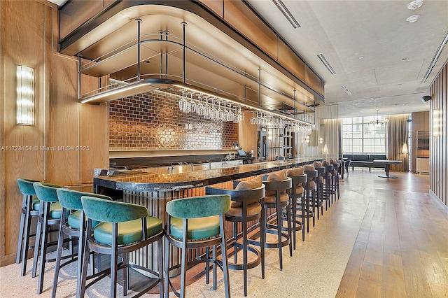 bar with brick wall, light wood-type flooring, a chandelier, and wooden walls