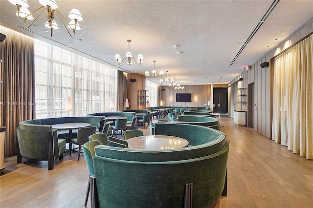 dining space with a chandelier, wood walls, light hardwood / wood-style floors, and a textured ceiling