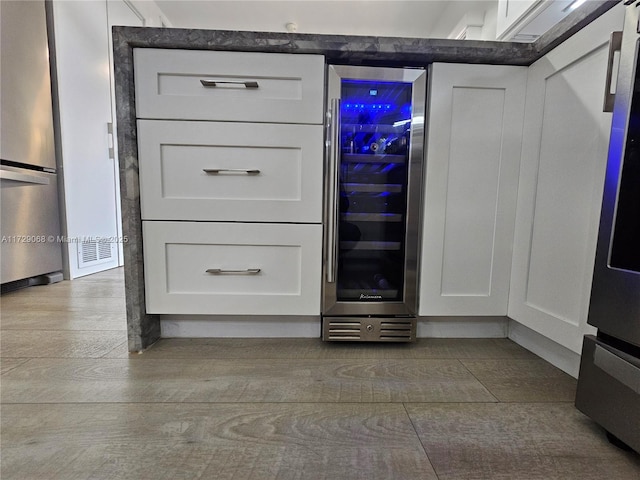 room details featuring white cabinets, beverage cooler, stainless steel refrigerator, and light hardwood / wood-style flooring