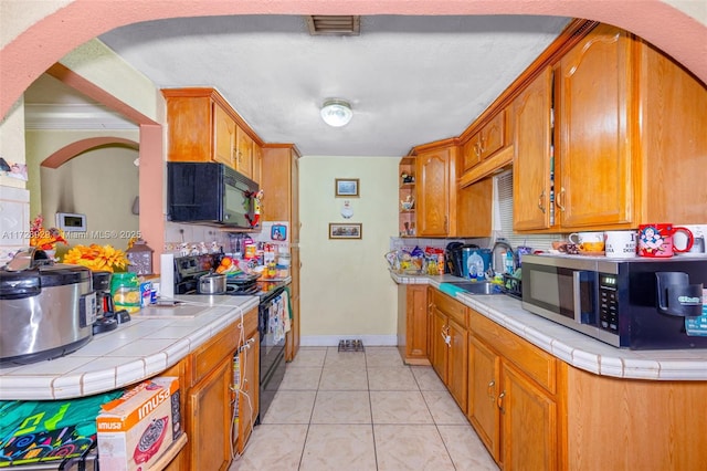 kitchen with light tile patterned floors, tile counters, black appliances, crown molding, and sink