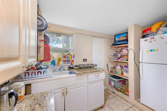 kitchen with white fridge, light tile patterned flooring, white cabinets, light stone counters, and sink