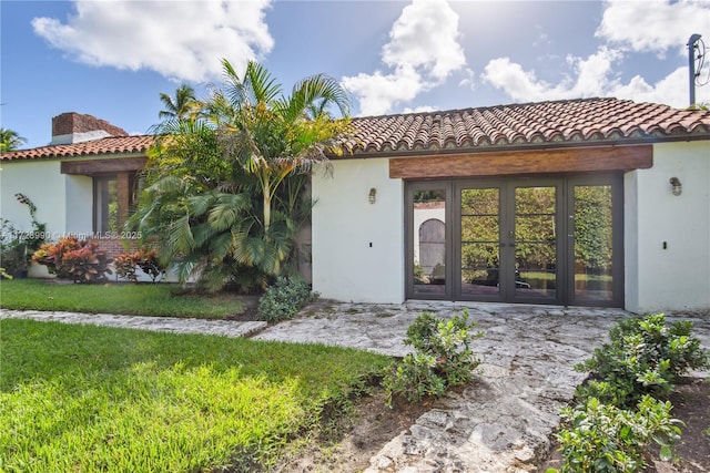 property entrance with stucco siding, a yard, french doors, and a tile roof
