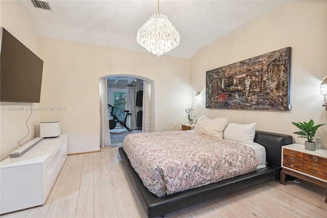 bedroom with a notable chandelier, visible vents, light wood-style flooring, baseboards, and arched walkways