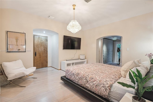 bedroom with a chandelier, arched walkways, and light wood-style floors
