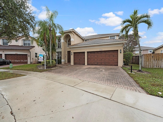 view of front of house featuring a tile roof, an attached garage, fence, decorative driveway, and stucco siding