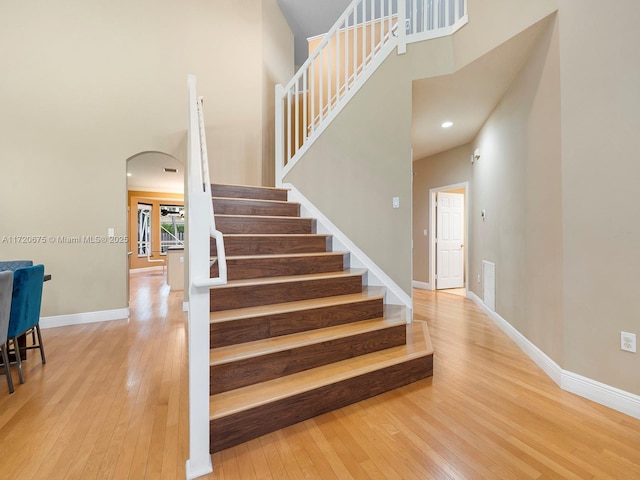 staircase with a towering ceiling, wood-type flooring, and baseboards