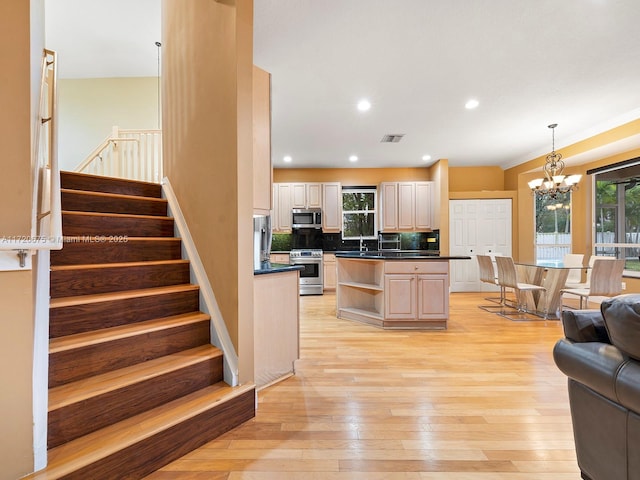 kitchen with a chandelier, light wood-style floors, appliances with stainless steel finishes, tasteful backsplash, and dark countertops