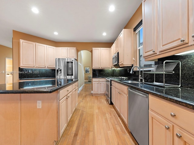 kitchen with decorative backsplash, dark stone counters, appliances with stainless steel finishes, light wood-style floors, and a sink