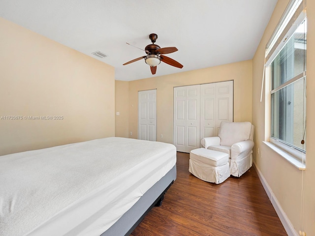 bedroom featuring two closets, visible vents, dark wood-type flooring, a ceiling fan, and baseboards