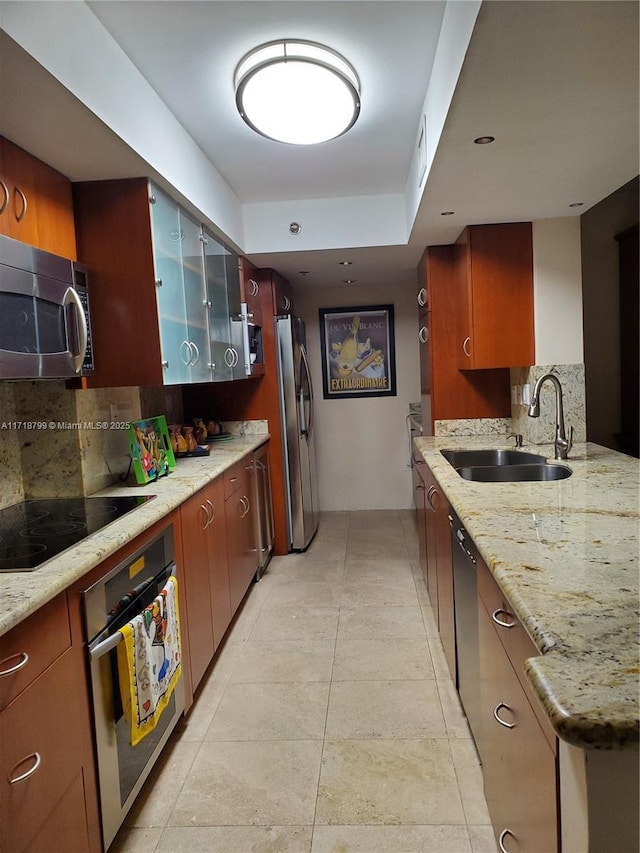 kitchen with light stone countertops, backsplash, appliances with stainless steel finishes, and sink