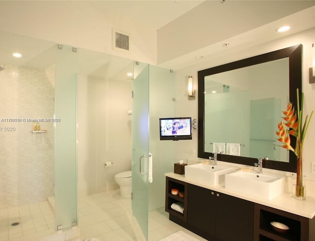 bathroom with toilet, vanity, a tile shower, and tile patterned flooring