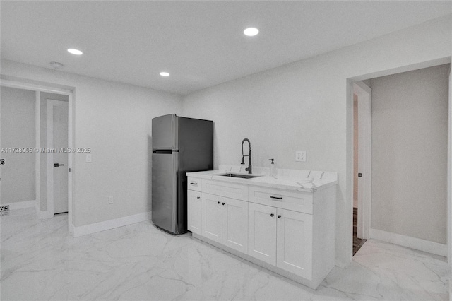 kitchen with light stone countertops, white cabinets, stainless steel fridge, and sink