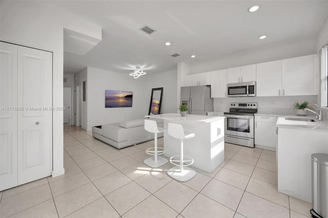 kitchen featuring a kitchen island, sink, light tile patterned floors, appliances with stainless steel finishes, and white cabinets