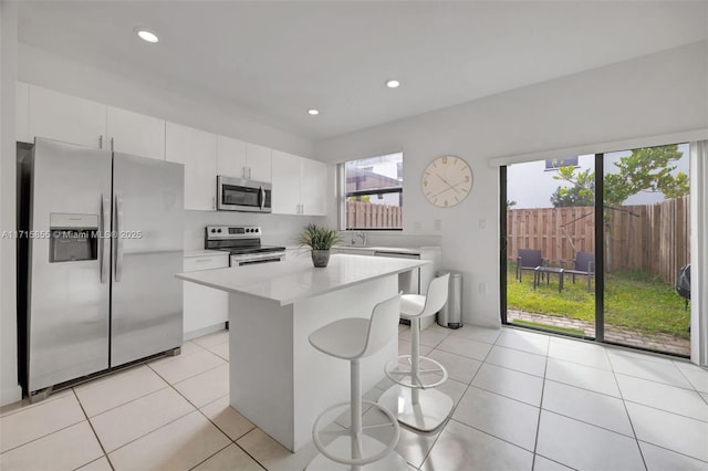 kitchen featuring white cabinets, appliances with stainless steel finishes, a center island, light tile patterned flooring, and a breakfast bar area