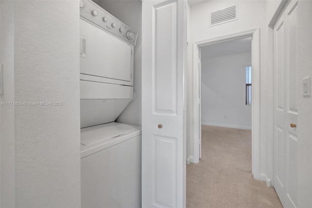 clothes washing area featuring stacked washer and dryer and light colored carpet