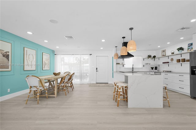 kitchen featuring pendant lighting, a breakfast bar area, white cabinetry, light stone counters, and light hardwood / wood-style floors