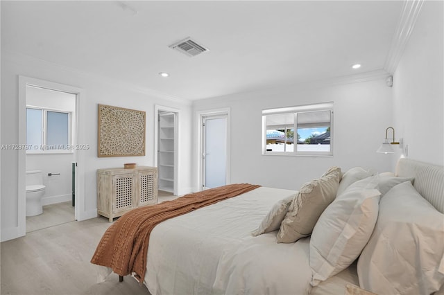 bedroom featuring crown molding, ensuite bath, light wood-type flooring, and a spacious closet