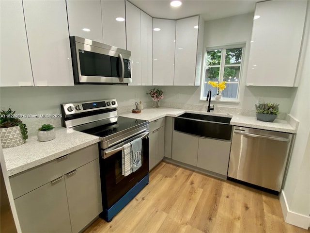 kitchen featuring sink, light wood-type flooring, light stone countertops, appliances with stainless steel finishes, and white cabinets