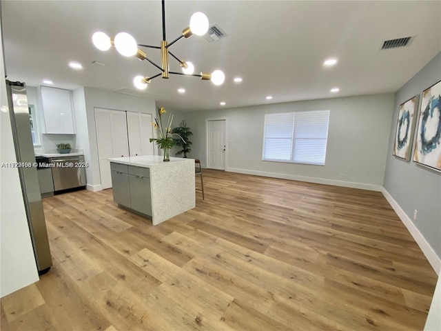 kitchen featuring white cabinets, a center island, decorative light fixtures, stainless steel refrigerator, and light hardwood / wood-style flooring