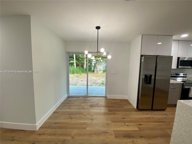 kitchen featuring appliances with stainless steel finishes, light hardwood / wood-style flooring, white cabinetry, and hanging light fixtures